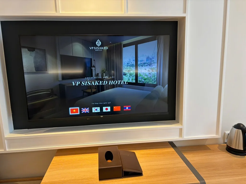 Smart TV trong phòng VP Sisaked Hotel ở Vientiane hiện màn hình chào với 6 lá cờ ngôn ngữ: Việt, Anh, Hàn, Nhật, Trung, Lào