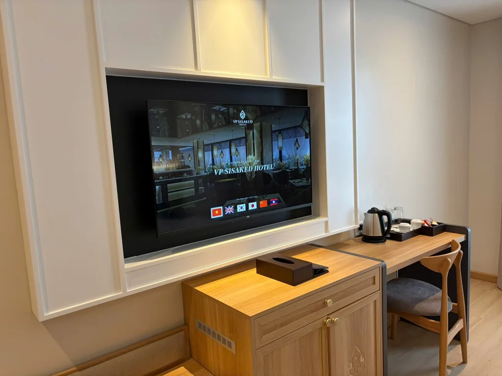 TV gắn âm tường phía trên bàn làm việc trong phòng VP Sisaked Hotel, màn hình IPTV đang hiện lời chào